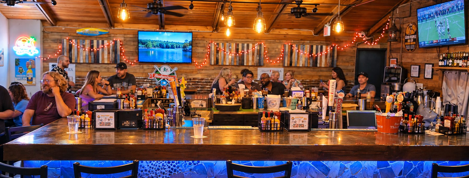 The bar at Drews Brews and Grille with guests seated along the counter, string lights, wood wall panels and TVs overhead