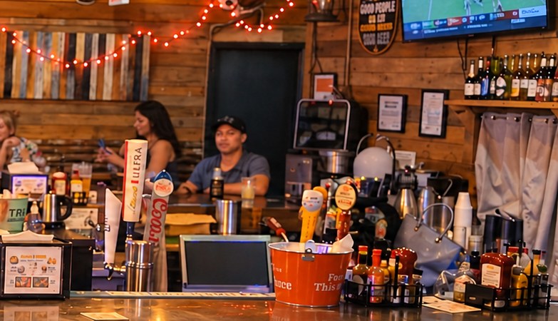 Beer tap handles, a bucket of condiments and bottles behind the bar at Drews