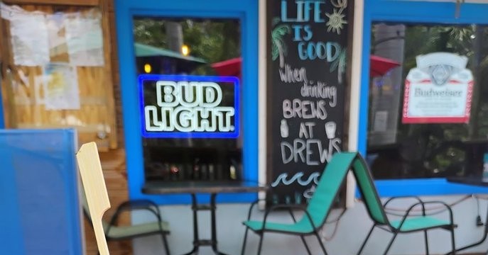 Porch at Drews with a lit Bud Light neon sign and a chalkboard reading 